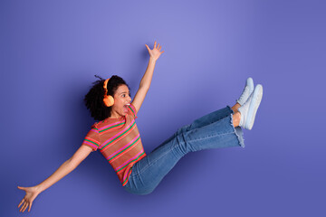 Smiling young woman wearing headphones gesturing joyfully against violet background for leisure and...