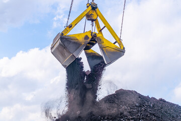 The bucket of the excavator crane pours coal from the bucket onto a large pile of coal. Coal...