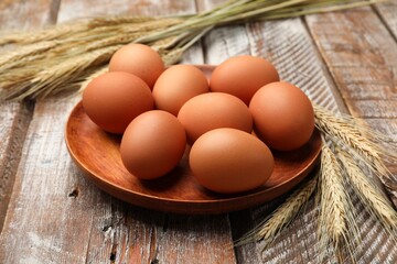 Raw eggs and spikes of wheat on wooden table, closeup