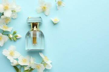 Bottle of perfume and beautiful jasmine flowers on light blue background, flat lay. Space for text