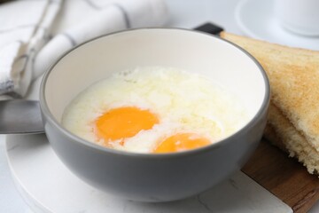 Half-boiled eggs in bowl and toasted bread on white tiled table, closeup. Traditional asian breakfast