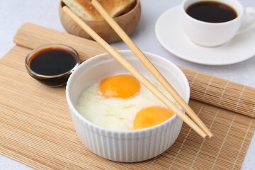 Half-boiled eggs in bowl, soy sauce, chopsticks, coffee and toasted bread on light grey table, closeup. Traditional asian breakfast