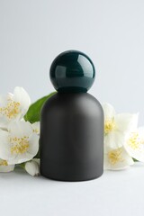 Bottle of perfume and jasmine flowers on light background, closeup