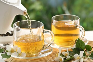 Pouring tasty jasmine tea into cup on white wooden table, closeup
