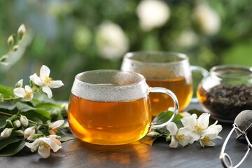 Tasty jasmine tea in cups, dry leaves and flowers on black table, closeup