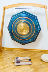 Hexagonal gong hangs on a wooden frame, accompanied by mallets resting on a cushion on the floor....
