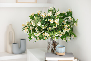Beautiful jasmine flowers in vase, books and decor on white cabinet indoors