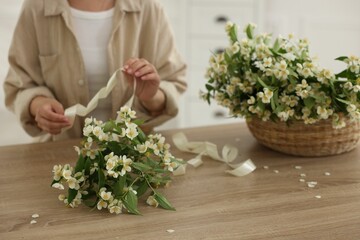 Woman making bouquet of jasmine branches at wooden table, closeup