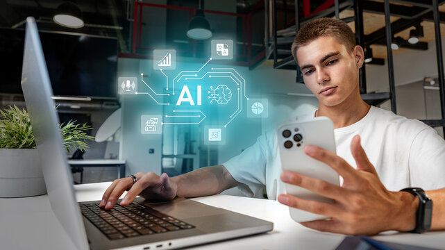 Young man engaged in artificial intelligence research while using a laptop and smartphone in a modern office space