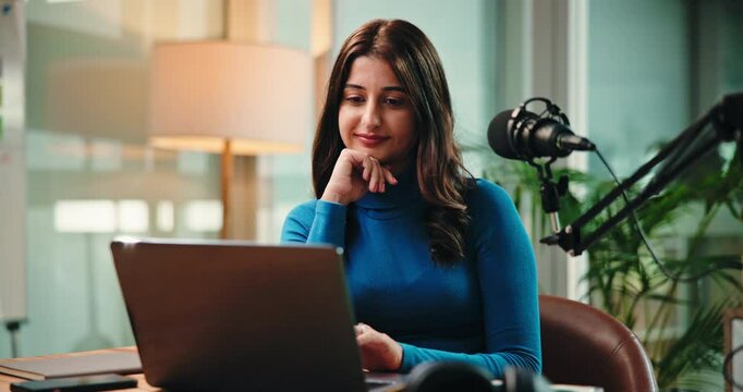 Online, laptop and woman with mic in studio for podcast, editing stream and recording with headphones. Content creation, journalism and person on computer for audio, radio presenter and hosting show