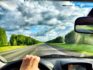 The driver steers along a highway, with vibrant green fields and dramatic clouds stretching across...