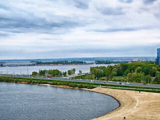 Coastal view of a riverbank with green trees and overcast skies near a city during early evening