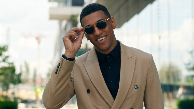 Smiling stylish fashionable confident African American business man posing in city outdoors wearing black sunglasses businessman guy male entrepreneur smile at camera in eyewear style fashion happy