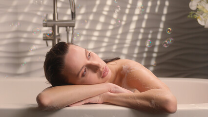 Pensive dreaming tranquil relaxed calm peaceful thinking woman Caucasian girl female lady relax in bathtub spa at home bath warm hot water hygiene pleasure enjoy beauty routine shower gel soup bubbles