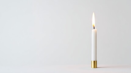 White candle with a golden base, softly glowing flame, placed on a minimalist surface, creating a serene atmosphere ideal for relaxation and meditation moments