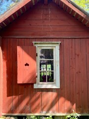 An old red plank wooden cottage. Finland. Red wood surface, weathered. White window