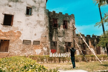  Scenic view of a man standing outside the Old Fort  - An abandoned historal building in Old Stone Town in Bagamoyo Town, Tanzania 
