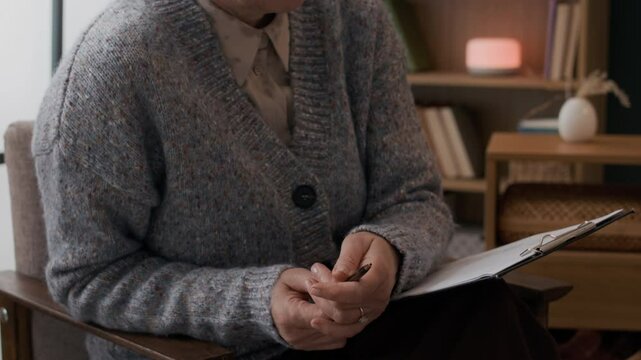 Slowmo tilt down shot of mature female psychologist in eyeglasses holding notes listening attentively to patient during therapy session in modern office