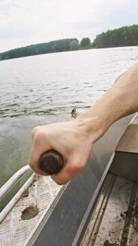 Close-up of a boatman's hand rowing through the water while sitting on a rowboat using a rowlock. vertical