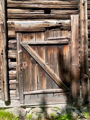 Weathered and aged wooden door with vintage rustic panel design in a country house or cabin exterior. Textured wooden grain and worn surface. Finland, 19th century