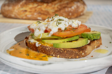 Delicious poached egg avocado toast with sliced tomatoes and herbs