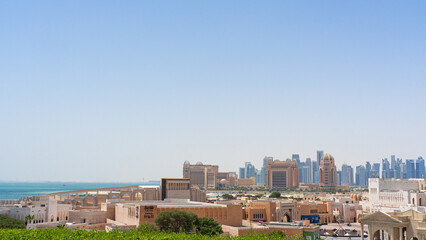 Panoramic view of Doha, Qatar, showingcasing traditional architecture, the Arabian Gulf, and the skyline under a clear blue sky.