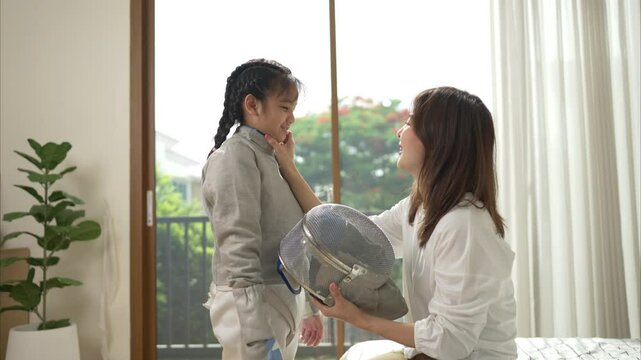 A girl in fencing gear with their mother preparing sports equipment before practicing fencing in preparation for the upcoming competition day