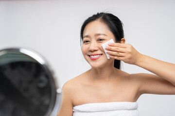 Happy asian woman looking at mirror and using cotton pad clean make up on her face