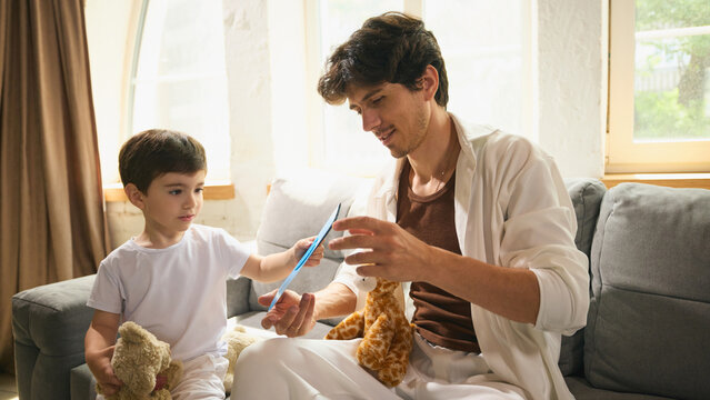 Little boy gives his dad a handmade Fathers Day card in light cozy atmosphere. Concept of family bonding through shared activities, gift ideas