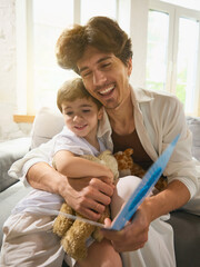 Father warmly embraces his young son on the couch after receiving a Fathers Day card. Concept of...