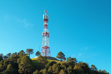 Obraz premium Tall communication tower stands prominently on hilltop against clear blue sky. Communication tower infrastructure contrasts with the natural landscape.