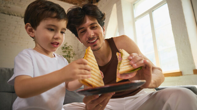 A white father and his young son share grilled sandwiches inside on Fathers Day. Highlights the theme of family connection and gratitude during a meaningful event.