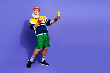 Funny man in retro athletic outfit posing energetically with a mobile phone against a solid purple background