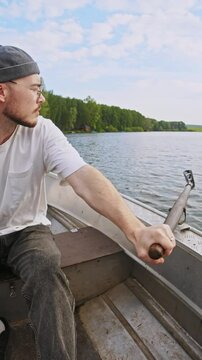 A young man, steering a boat, turns it around by using one oar to row while sailing on a lake.