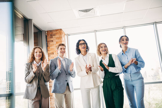 Group of professional coworkers applauding during a team meeting in a modern office space, celebrating success