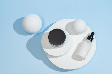 White skincare serum dropper bottle and cream jar on round white podium clean beauty packaging...
