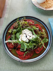 Top view of fresh Stracciatella salad with ripe tomatoes and olive oil drizzle rustic Italian appetizer flat lay