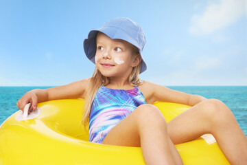 Cute little girl with sunscreen on her skin and inflatable ring in sea. Sun protection while...