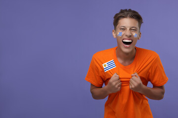 Excited fan with flags of Uruguay on his face and t-shirt against dark violet background. Space for...