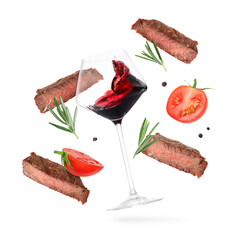 Red wine in glass, grilled beef meat, tomatoes and spices falling on white background