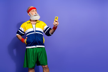 Elderly sportsman in retro activewear poses confidently while holding a smartphone, showcasing a fun