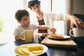 Daily Fatherhood. Caucasian dad and his child share a breakfast in a well-lit kitchen setting,...