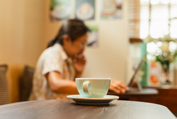 Selected focus cup of coffee on table with woman working on laptop in blur background.