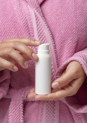 Closeup of woman in pink bathrobe holding white one pump cream tube in hands, cosmetic mockup