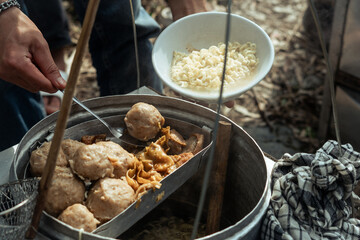 Street food vendor preparing traditional meatball soup with noodles in a bowl, a popular Asian culinary experience.