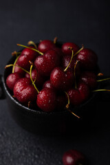 Juicy ripe fresh cherries with water drops in a black plate on a black background. Seasonal fruits, harvest. Selective focus, close-up.