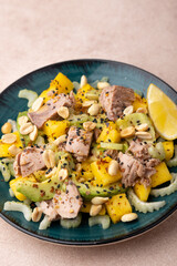 Salad with canned tuna, peanuts, mango, avocado, celery, chili flakes and black sesame. Light summer salad with olive oil and a lemon lobule. Home cooking. Selective focus, close-up.