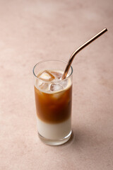 Coffee with coconut milk and ice cubes in a tall glass. Traditional non-alcoholic cold drink. In the background, a jar of coffee and a jar of sugar. Selective focus, close-up.