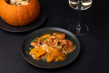 Whole baked pumpkin with tiger prawns, melted cheese, tomatoes and a glass of white wine. Traditional dish of Brazil, home cooking. Selective focus, close-up, black background.