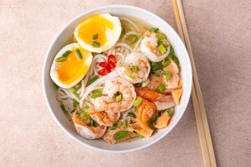 Asian dish with broth, noodles, tiger shrimp, fish, egg and green onions. Traditional Asian soup in a white deep plate. Selective focus, close-up.